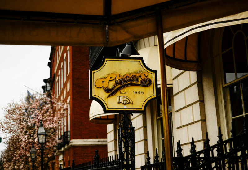 The iconic Cheers bar sign in Boston, reading 'Cheers Est. 1895', hanging over the entrance