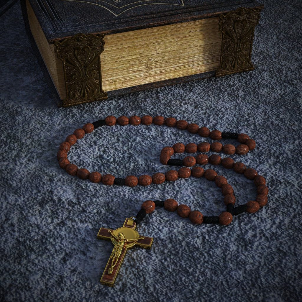 A worn rosary with a crucifix coiled on a table beside an old leather-bound prayer book